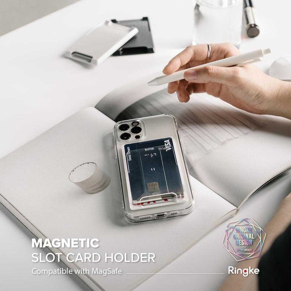 Card Holder | Magnetic Slot - A clear phone case with a magnetic card holder attached, resting on an open notebook with a pen.