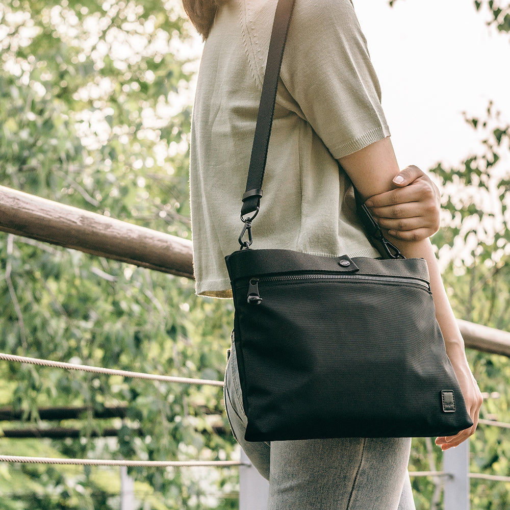 2-Way Bag - Person wearing a black crossbody bag with a zippered front pocket and adjustable strap outdoors.