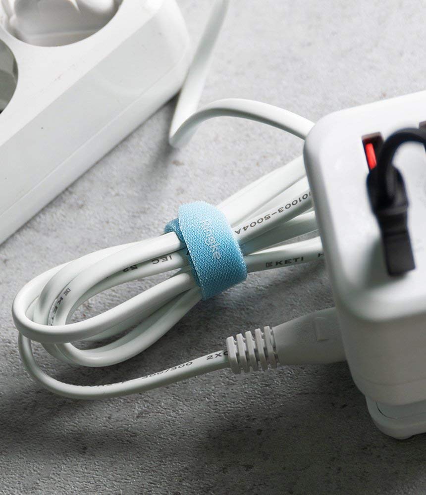Magic Cable Tie - A light blue velcro strap securing a coiled white power cord next to a white electrical outlet.