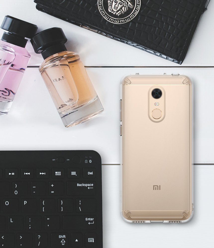Redmi Note 5 / 5 Plus | Fusion - Gold smartphone in a clear case on a white desk with perfume bottles and a keyboard.