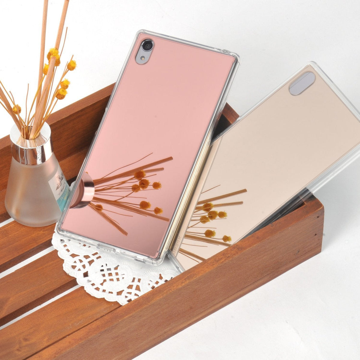 Xperia Z5 Premium Case | Mirror - Rose Gold - Two reflective rose gold phone cases resting in a wooden tray with a reed diffuser.