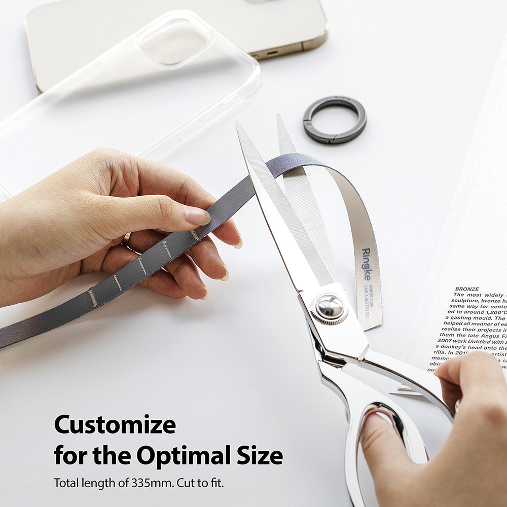 Ring Band Strap - Hands using scissors to cut a grey fabric strap to size on a white desk with a phone case and ring.