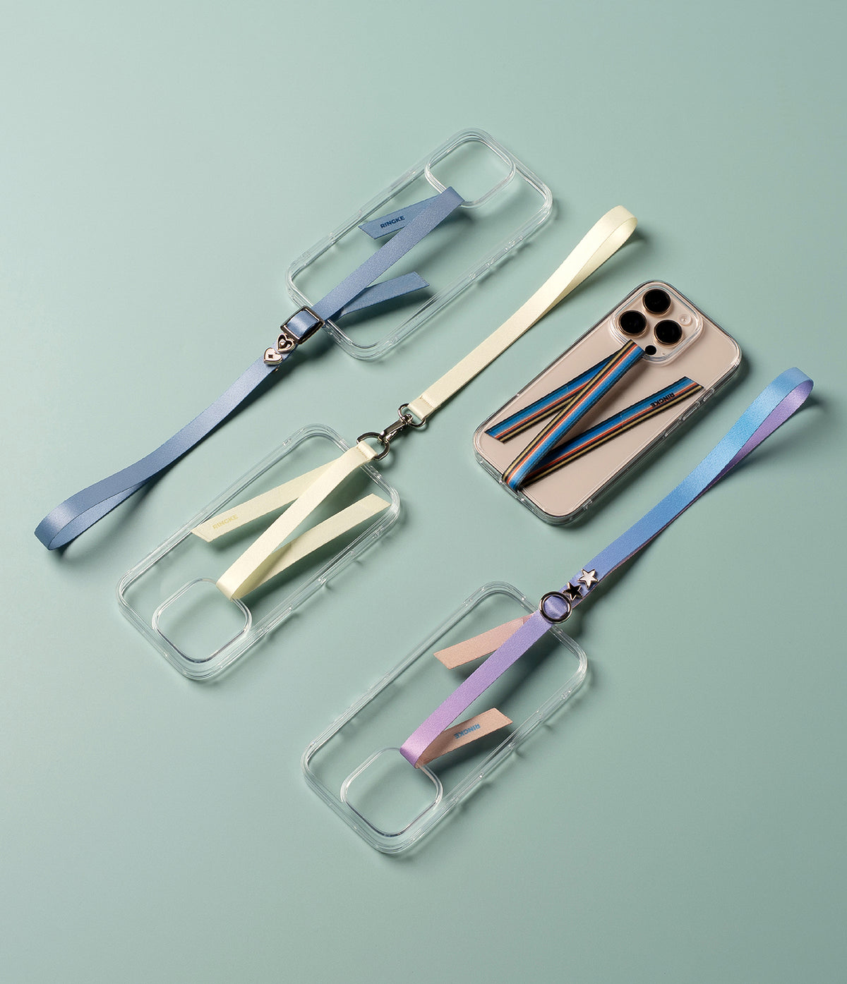 Band Strap - Three clear phone cases with colorful fabric hand straps featuring metal charms on a light green background.