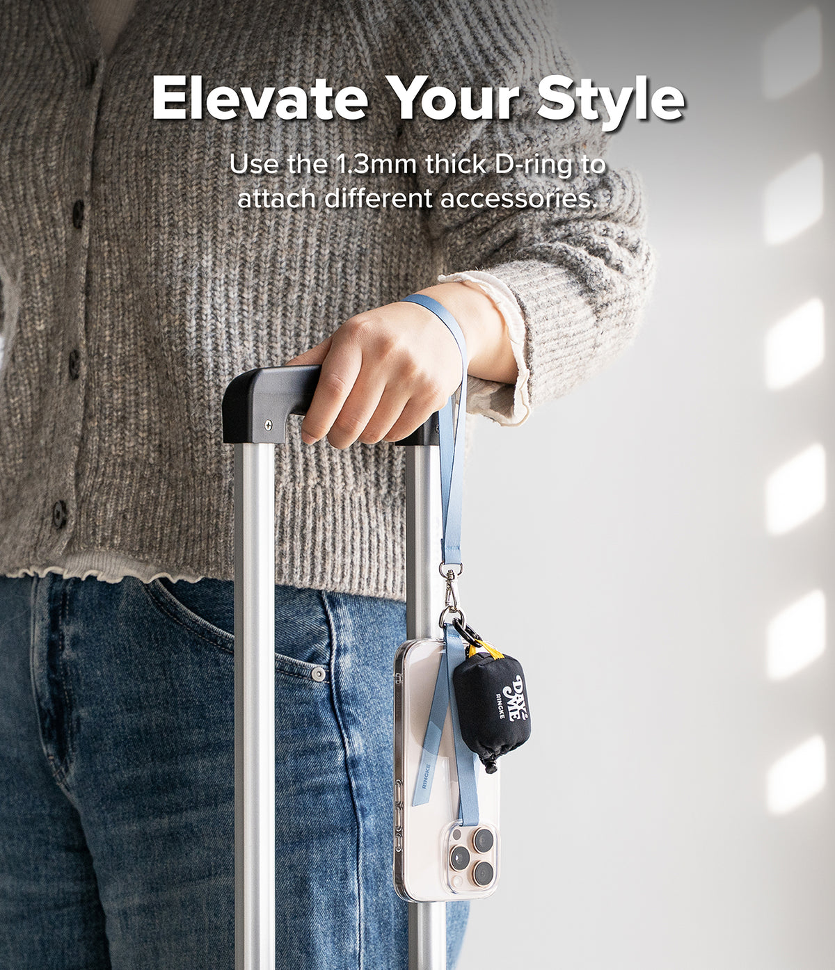 Band D Ring Hand Hook Strap - A person holding a suitcase handle with a blue wrist strap attached to a phone and pouch.