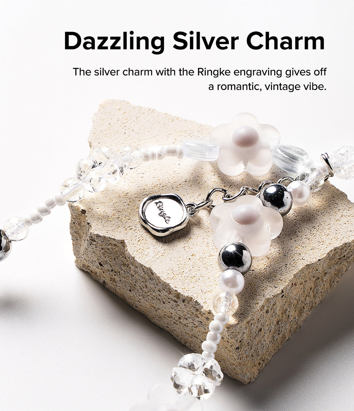 Beaded Strap - A beaded phone strap with flower charms and a silver Ringke-engraved pendant resting on a textured stone.