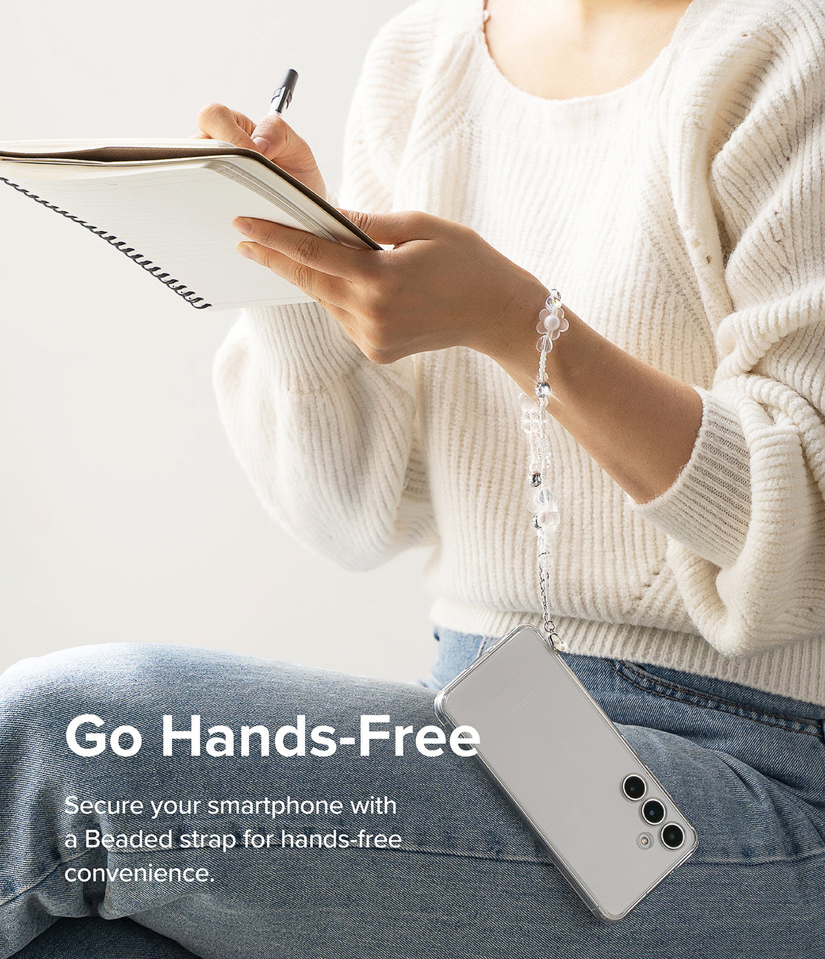 Beaded Strap - A person in a white sweater writes in a notebook while wearing a floral beaded phone strap on their wrist.