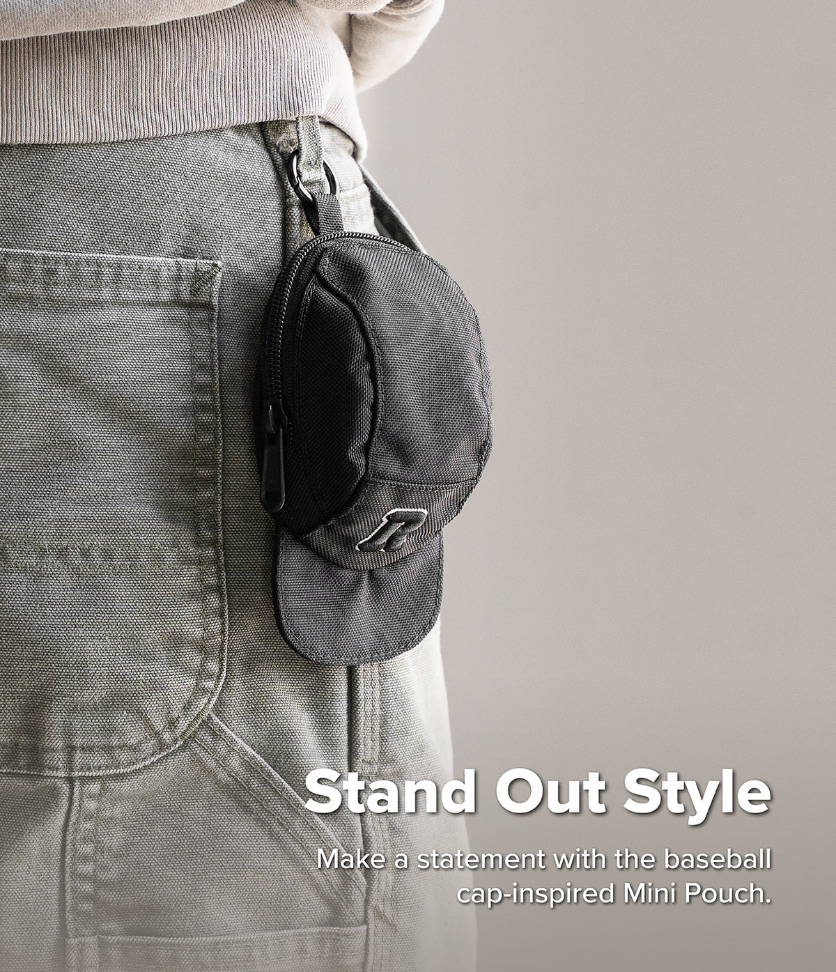 Mini Pouch | Cap - A black baseball cap-shaped mini pouch clipped to the belt loop of grey canvas pants.