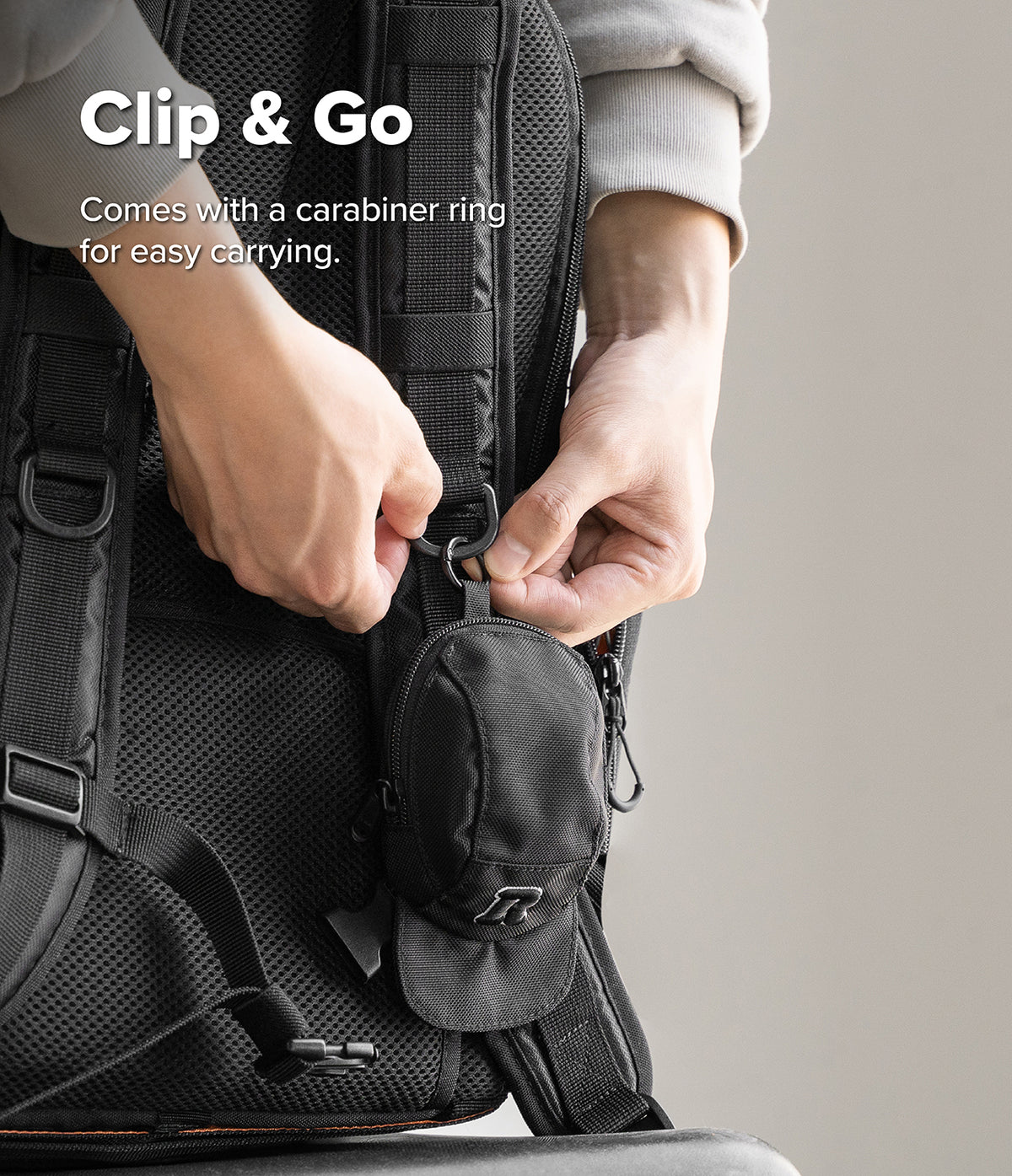 Mini Pouch | Cap - Hands attaching a small black cap-shaped pouch to a backpack strap using a carabiner ring.