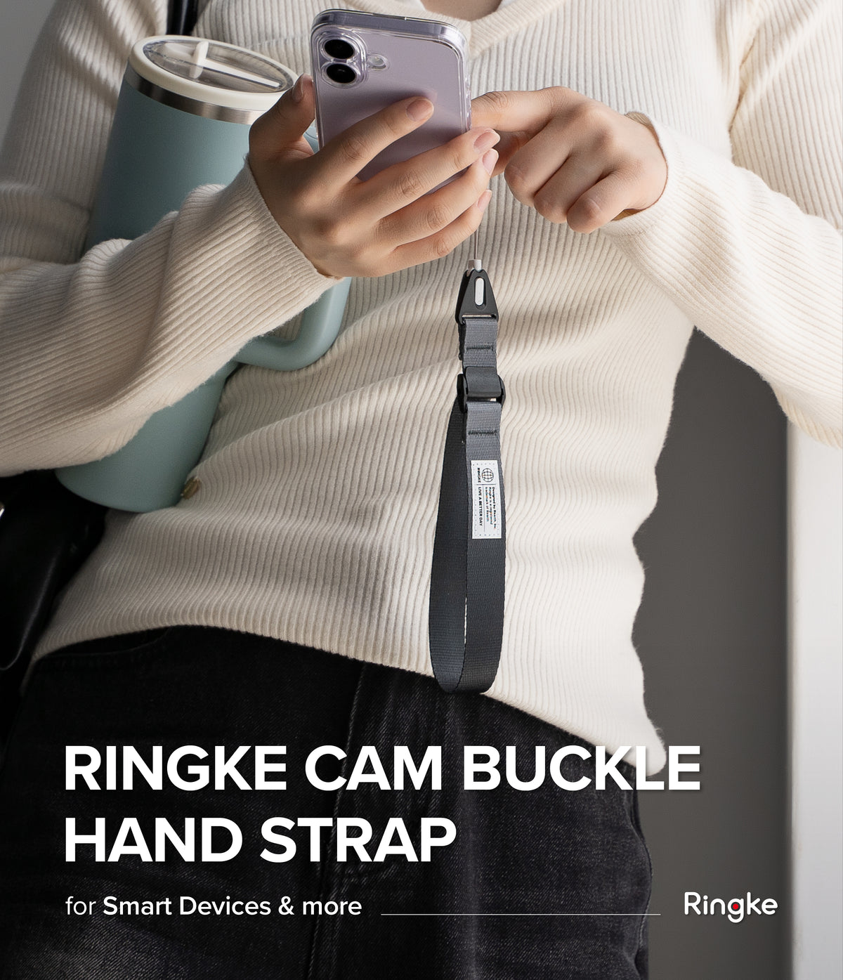 Cam Buckle Hand Strap - Person holding a phone with a Ringke cam buckle hand strap, wearing a beige sweater and black pants.