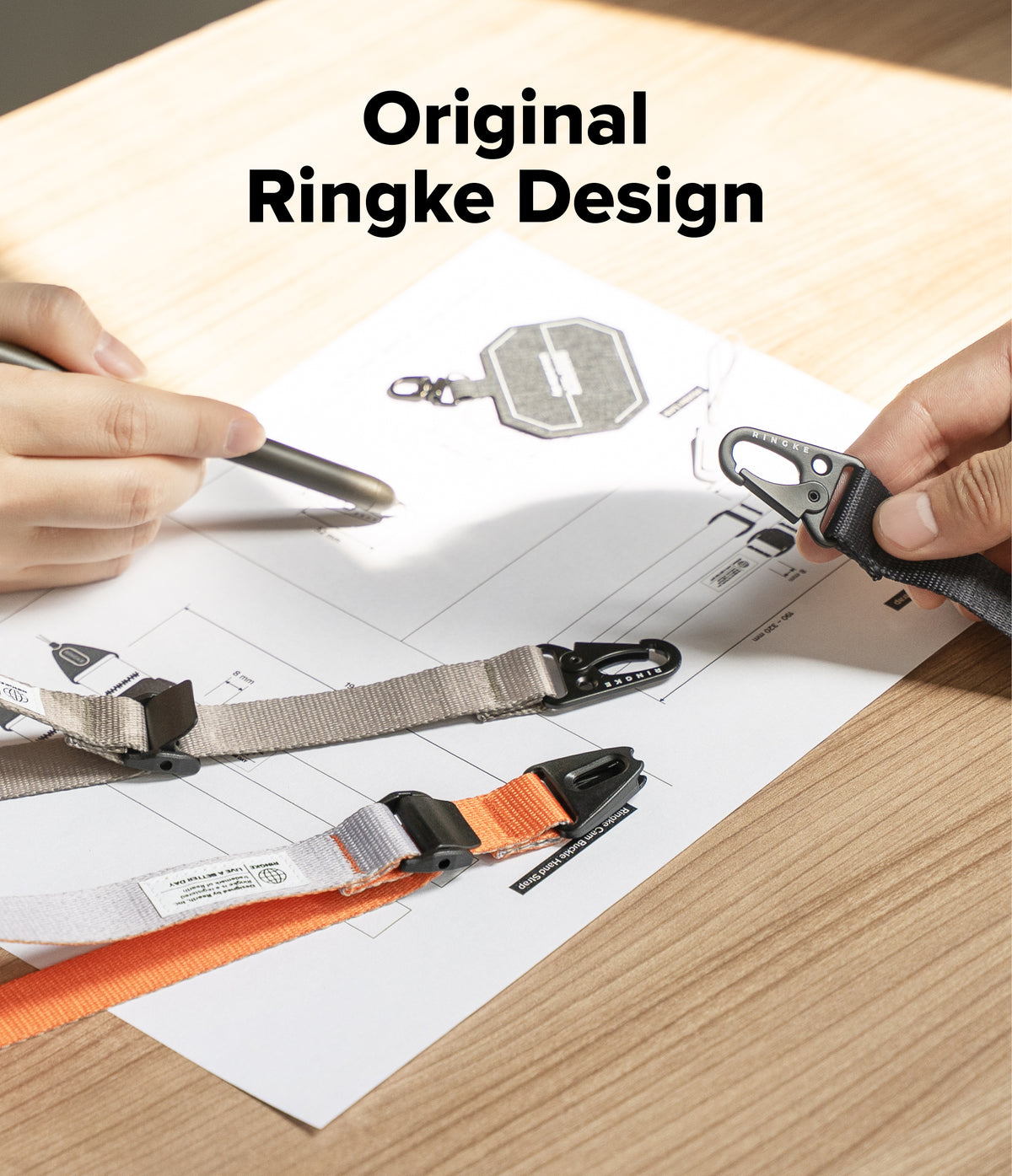 Cam Buckle Hand Strap - Person holding a keychain with 'Original Ringke Design' text on a desk.