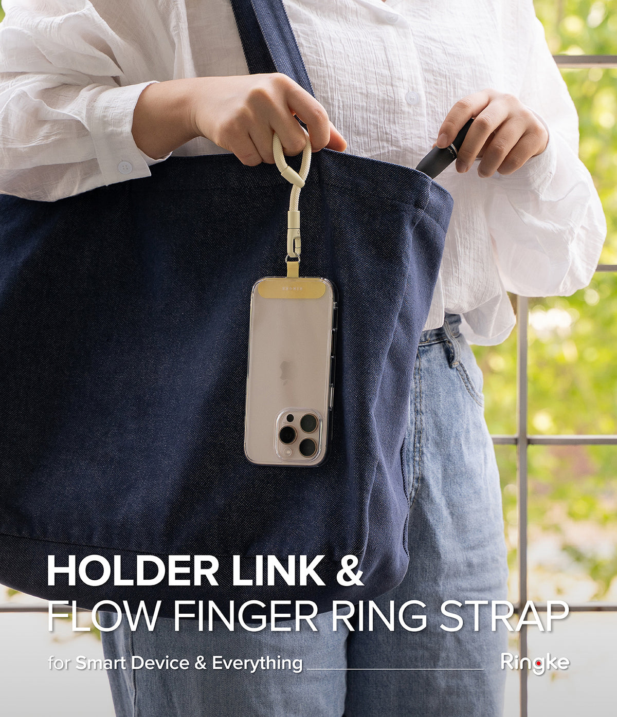 Holder Link Flow Finger Ring - A person holding a phone attached to a cream-colored finger strap hanging from a blue tote bag.