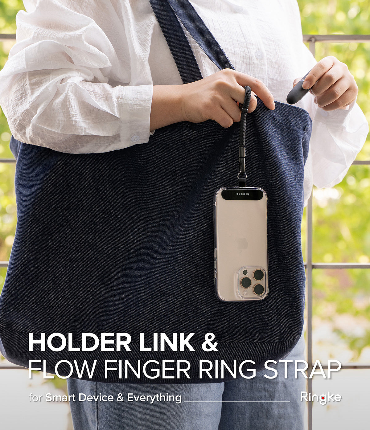 Holder Link Flow Finger Ring - A person holding a black finger ring strap attached to a smartphone hanging from a denim tote bag.