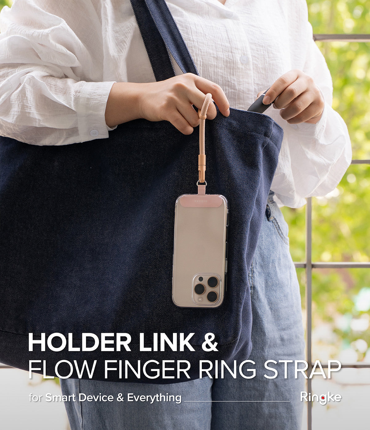 Holder Link Flow Finger Ring - A person holding a phone attached to a beige finger ring strap hanging from a denim tote bag.