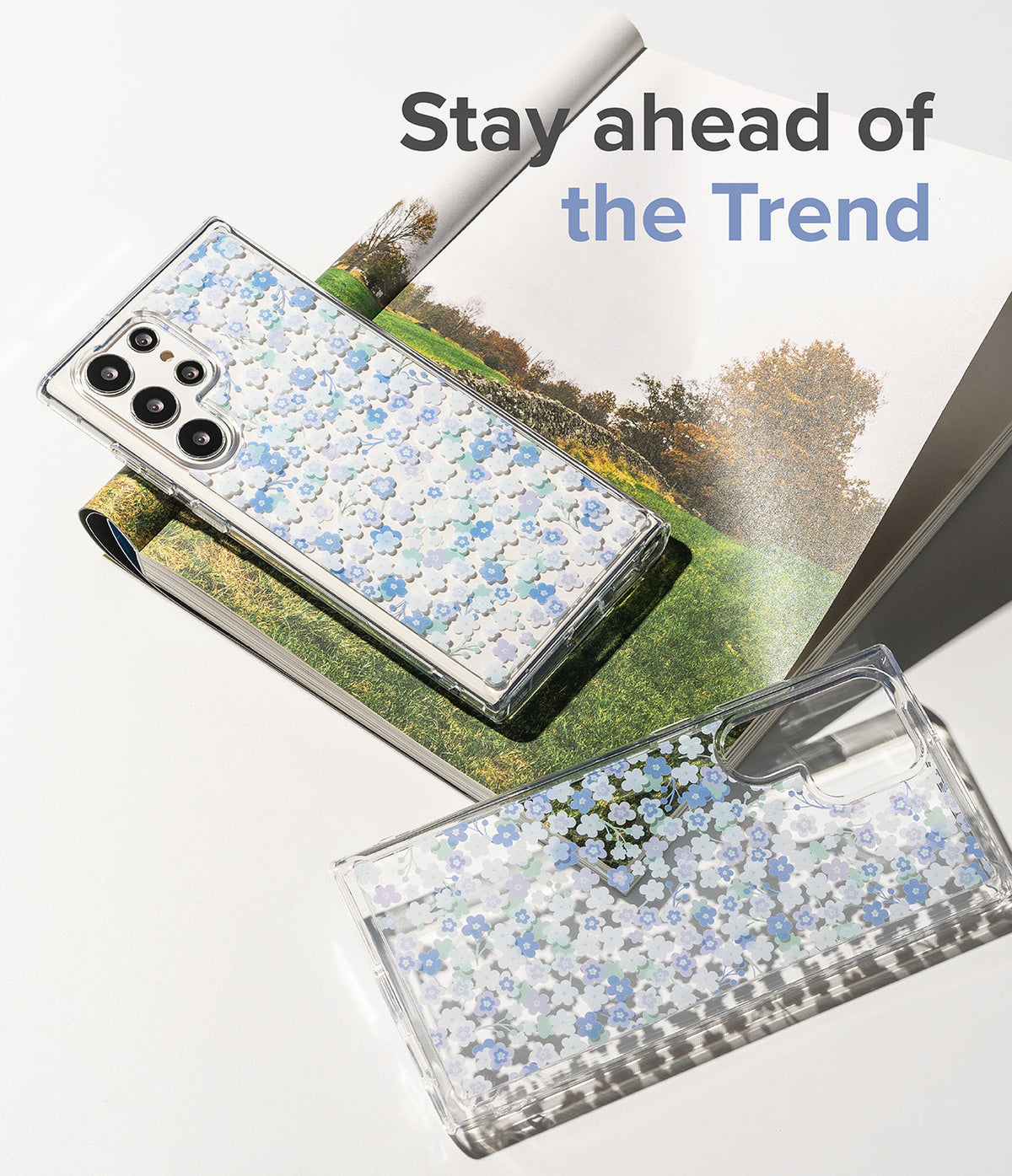 Galaxy S22 Ultra Case | Fusion Design - Two clear phone cases with blue floral patterns resting on a magazine.