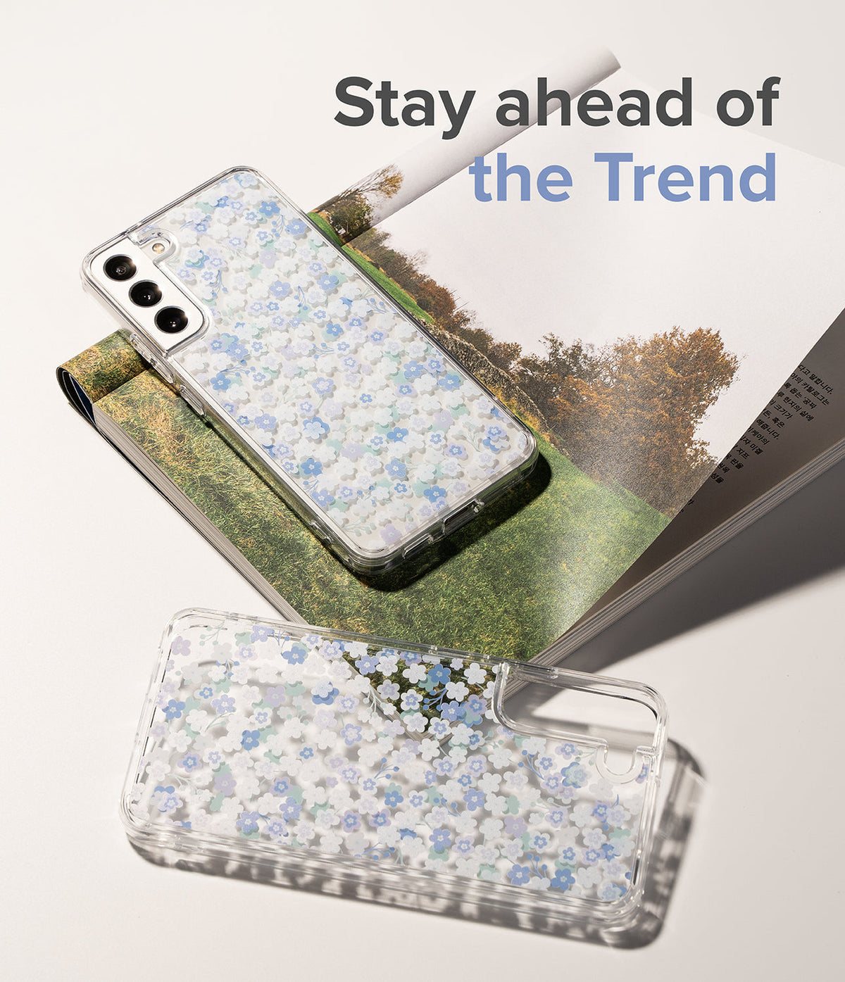 Galaxy S22 Case | Fusion Design - Two clear phone cases with blue and white floral patterns resting on an open magazine.