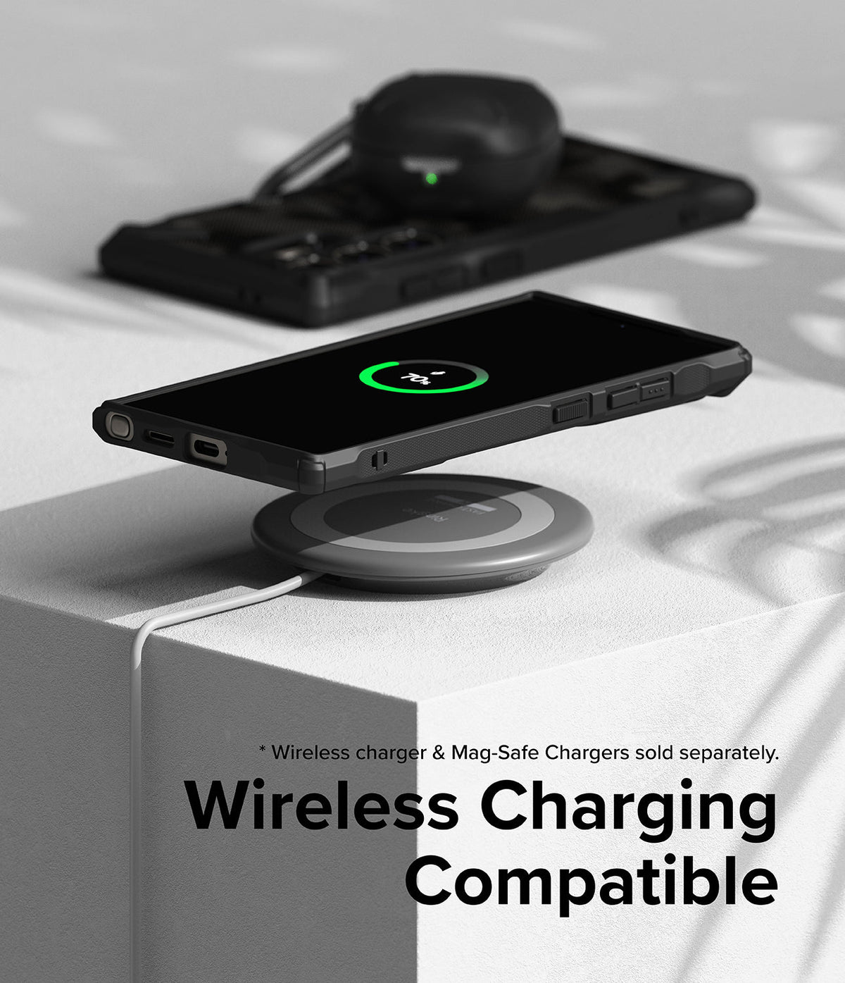 Galaxy S24 Ultra Case | Fusion-X - Phone in a black case wirelessly charging on a pad with earbuds in the background.
