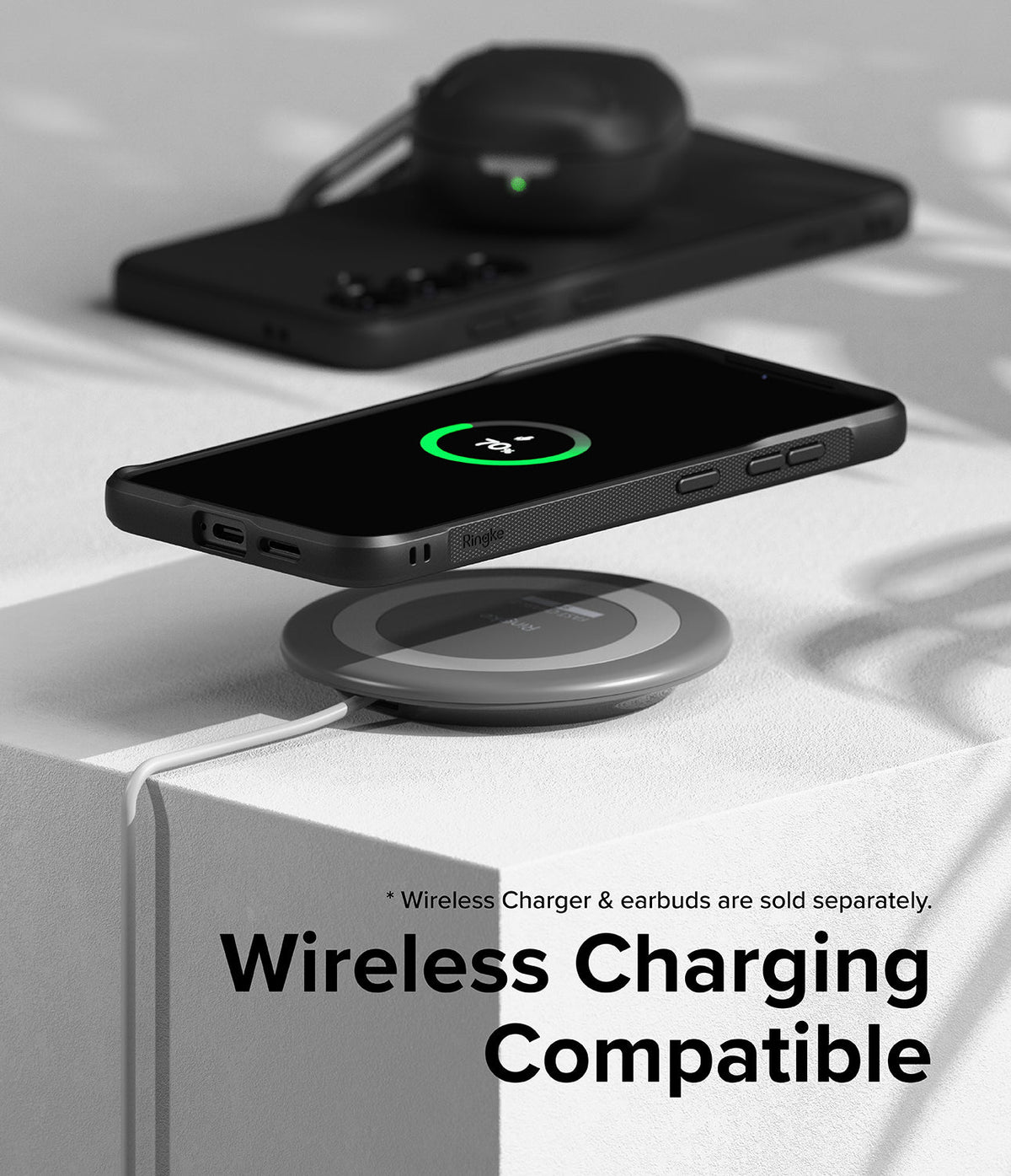 Galaxy S24 Case | Onyx - Black phone in Onyx case wirelessly charging on a circular pad with earbuds in the background.