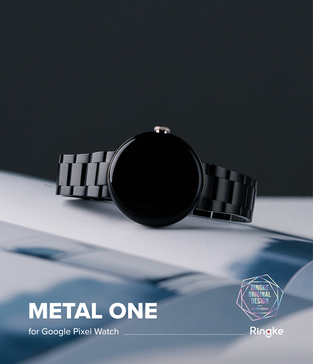 Google Pixel Watch | Metal One Band - Black smartwatch with a matching metal link band resting on a white surface.