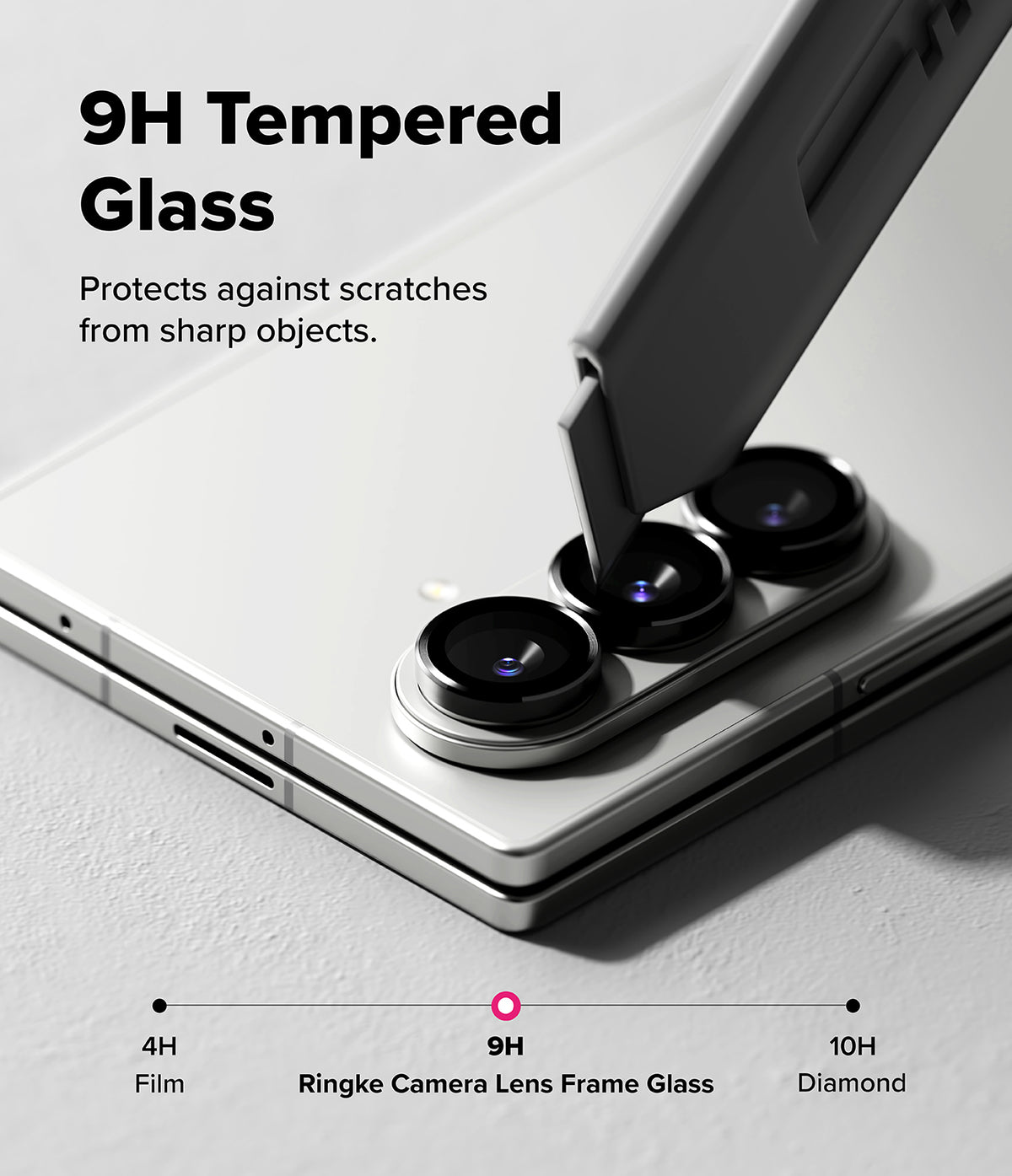 Galaxy Z Fold 7 | Camera Lens Frame Glass (2 Pack) - A utility knife blade scrapes against the 9H tempered glass camera lens protector on a silver smartphone.