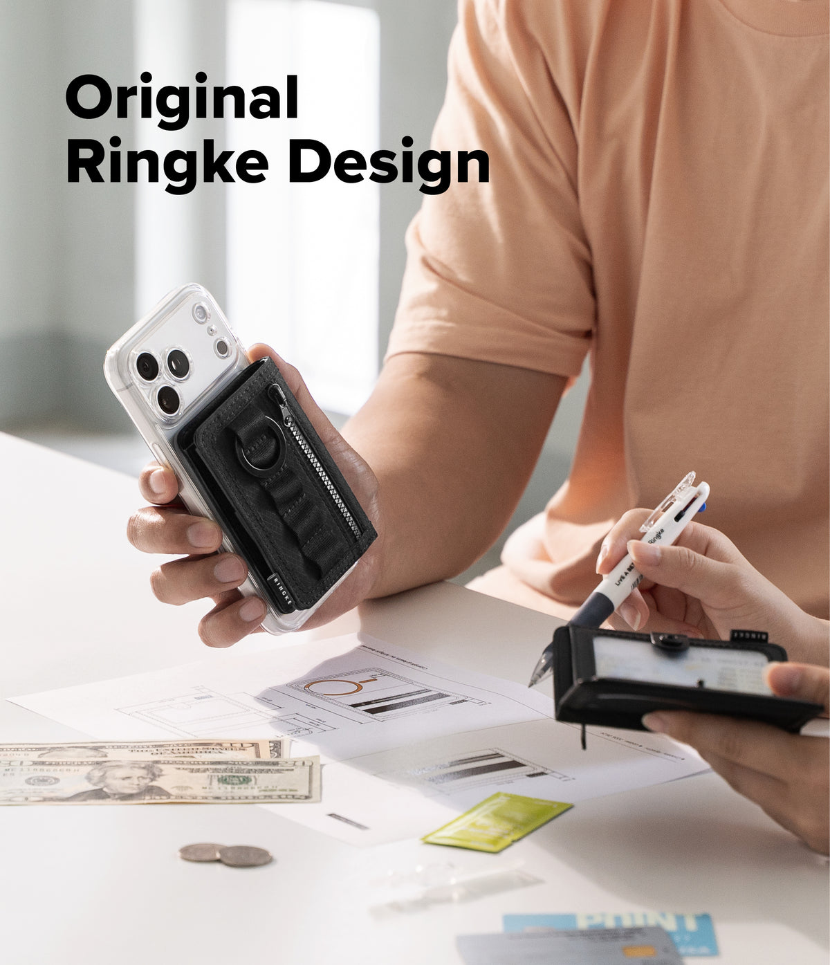 Wallet | Tech Magnetic - A person in a peach shirt holds a black Ringke-style phone accessory with a clear case in one hand while another hand uses a pen on a small black device at a white desk. Large text reads 'Original Ringke Design' in the upper left.