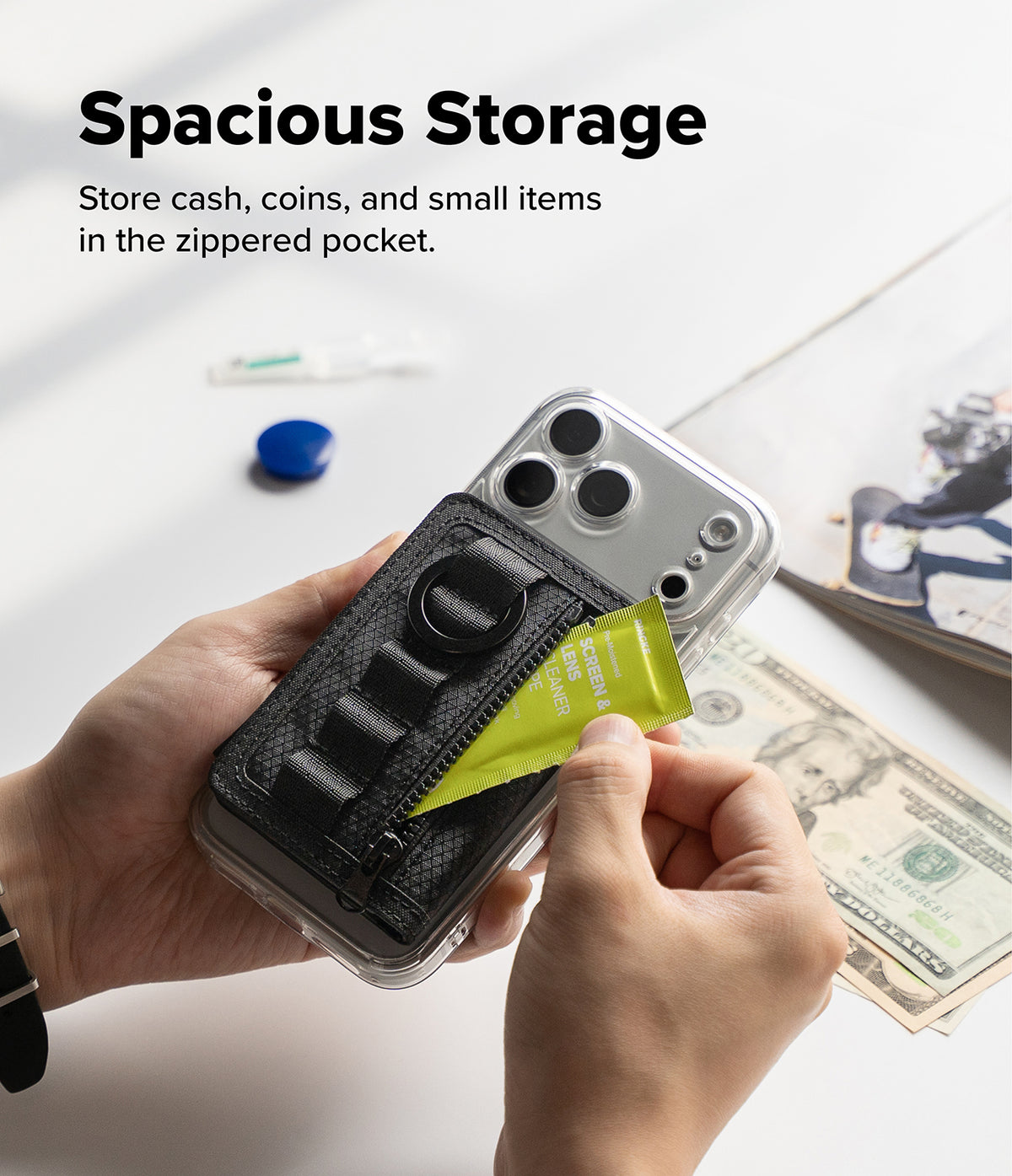 Wallet | Tech Magnetic - A clear phone case with a black zippered pocket and ring holder, held in two hands to demonstrate storage space. The text 'Spacious Storage' is displayed at the top, with cash and a magazine in the background to illustrate use cases.