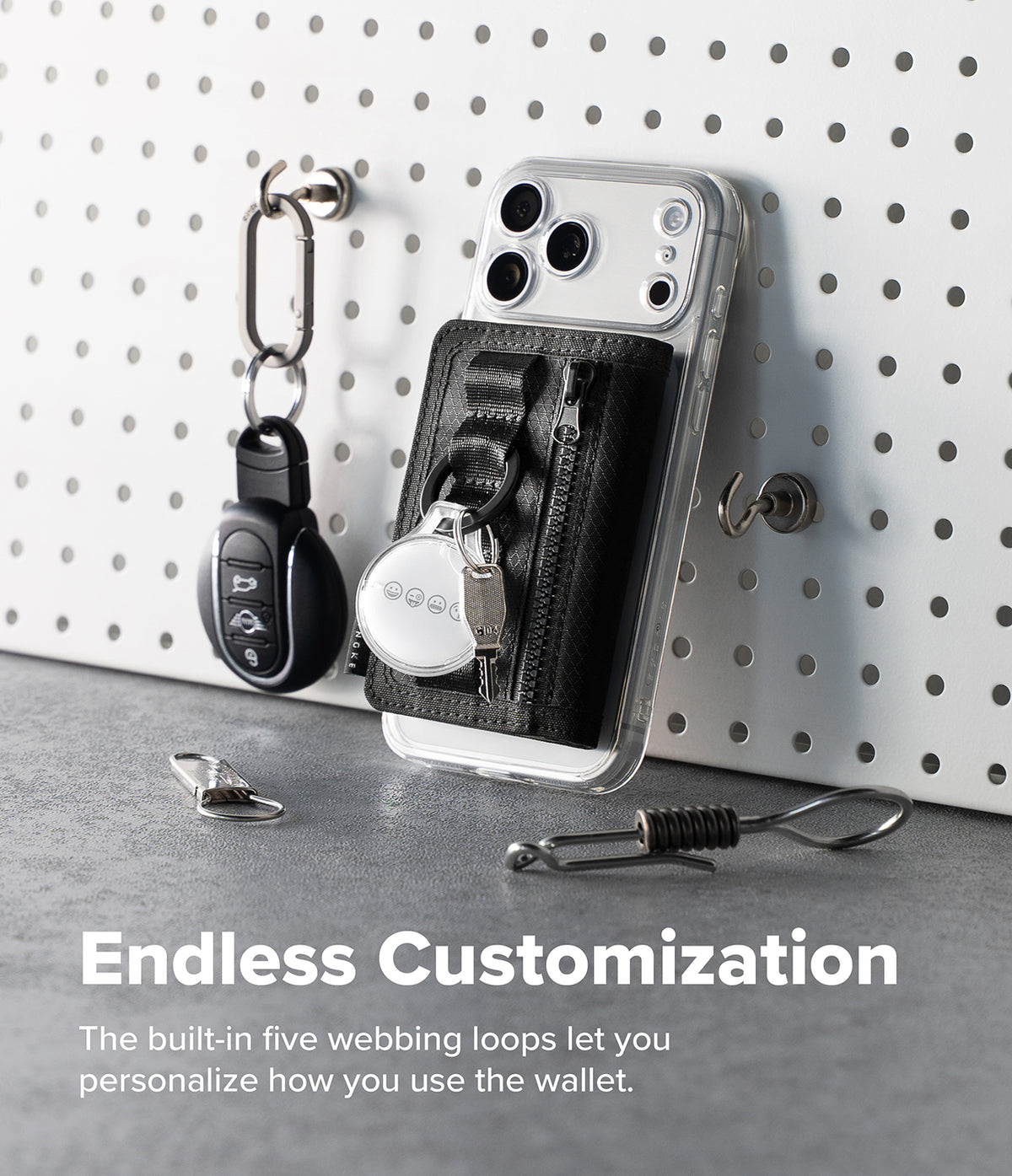 Wallet | Tech Magnetic - A clear smartphone case with a black built-in key wallet and zipper pocket, shown leaning against a white pegboard with keys hanging nearby. Text at the bottom reads 'Endless Customization' and describes the five webbing loops for personalization.