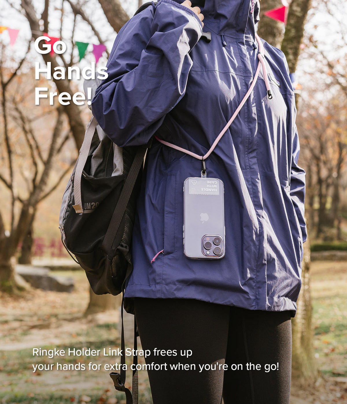 Holder Link Strap | Clear - Person wearing a clear phone case on a pink neck strap over a blue jacket in a park.
