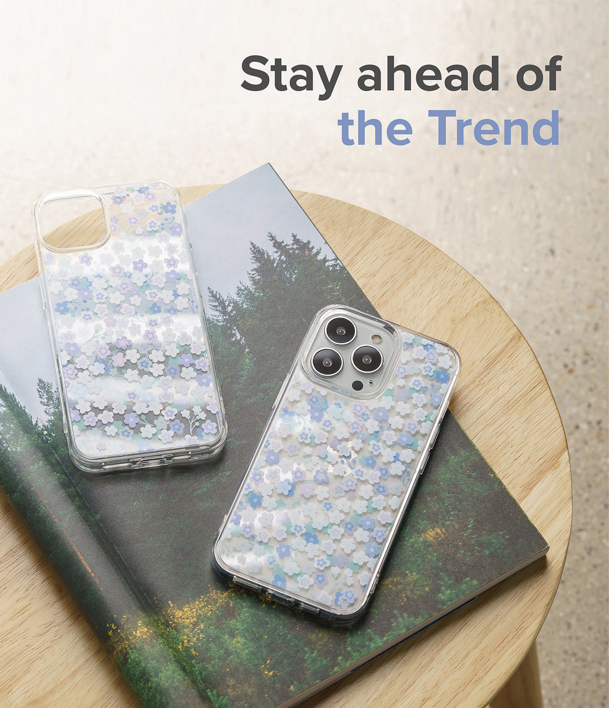 iPhone 13 Pro Max Case | Fusion Design - Two clear floral phone cases resting on a forest-themed book on a wooden stool.