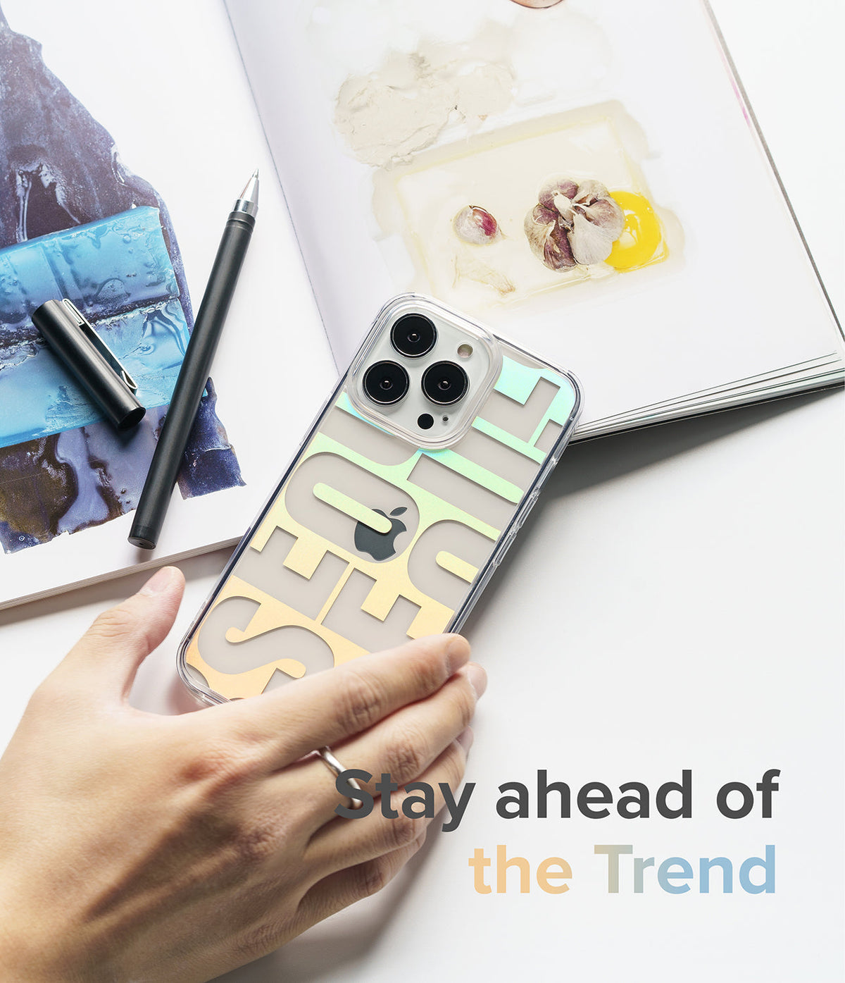 iPhone 13 Pro Case | Fusion Design - Hand holding a clear phone case with iridescent Seoul typography over an open art book.