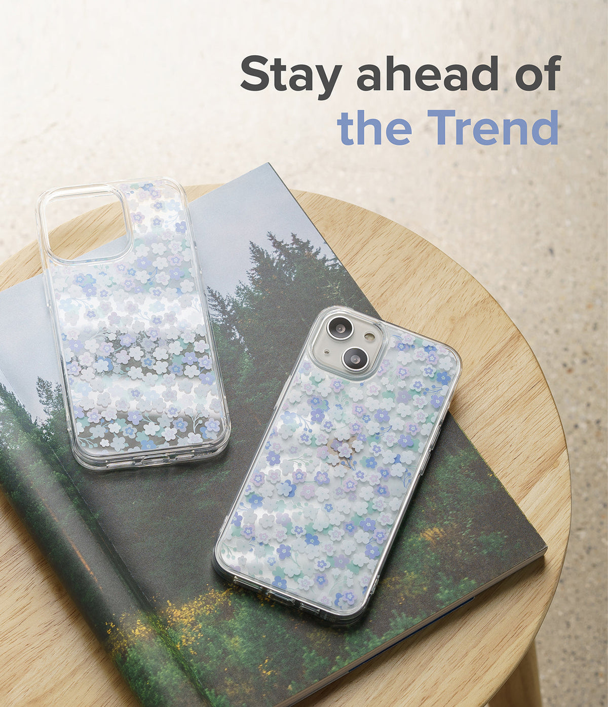 iPhone 13 Case | Fusion Design - Two clear phone cases with blue and white floral patterns resting on a forest-themed book.