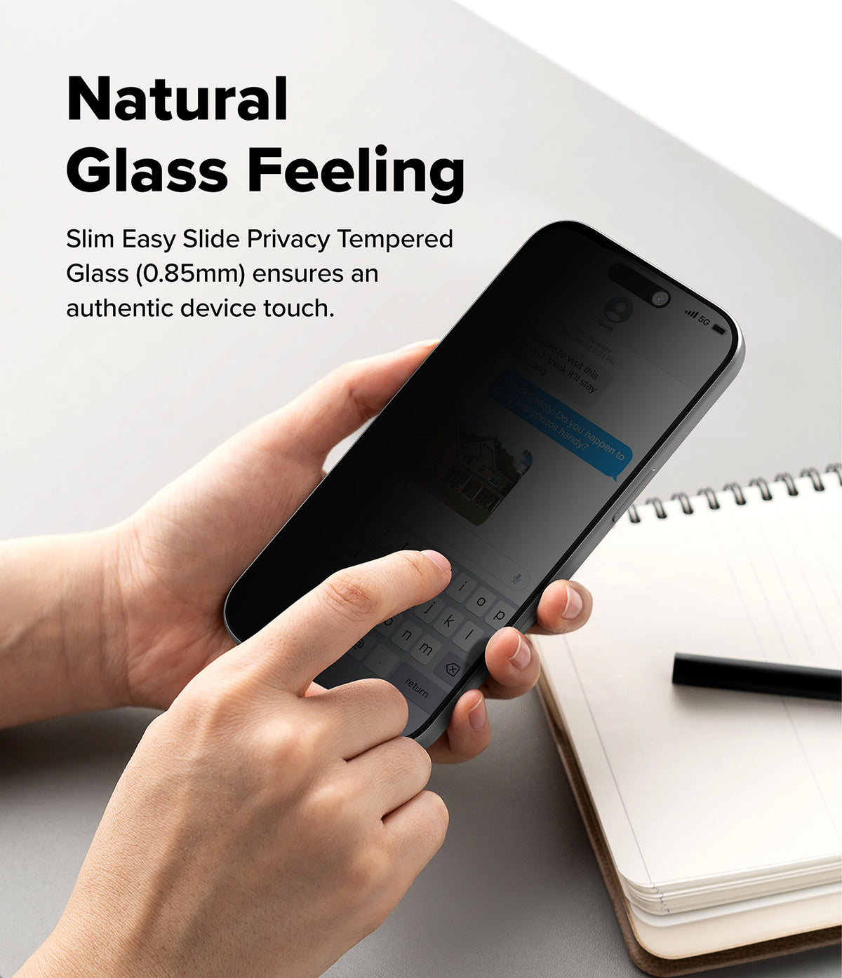 iPhone 18 Pro Max Screen Protector | Easy Slide Privacy Tempered Glass (2 Pack) - A person holds a smartphone with a dark privacy screen protector in both hands over a light gray desk, with a notebook and pen nearby. Text on the left reads 'Natural Glass Feeling' and describes slim easy slide privacy tempered glass.