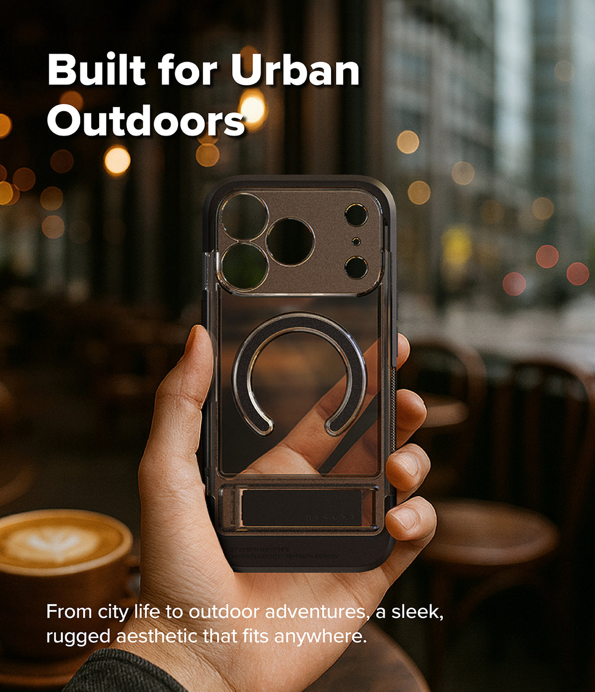 iPhone 18 Pro Max Case | UX Magnetic - A hand holds a dark gray rugged phone case with a built-in ring stand in a blurred cafe setting. Text on the image reads 'Built for Urban Outdoors' and 'From city life to outdoor adventures, a sleek, rugged aesthetic that fits anywhere.