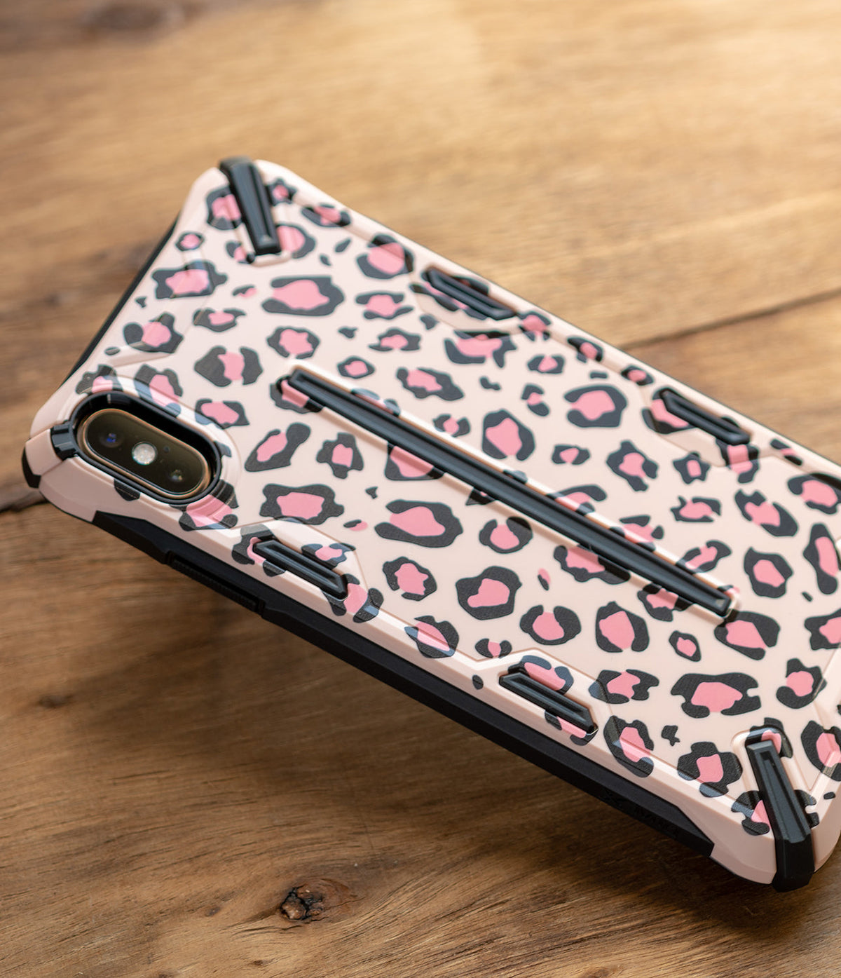 iPhone XS Max Case | Dual-X Design - Pink leopard print phone case with black protective bumpers on a wooden surface.