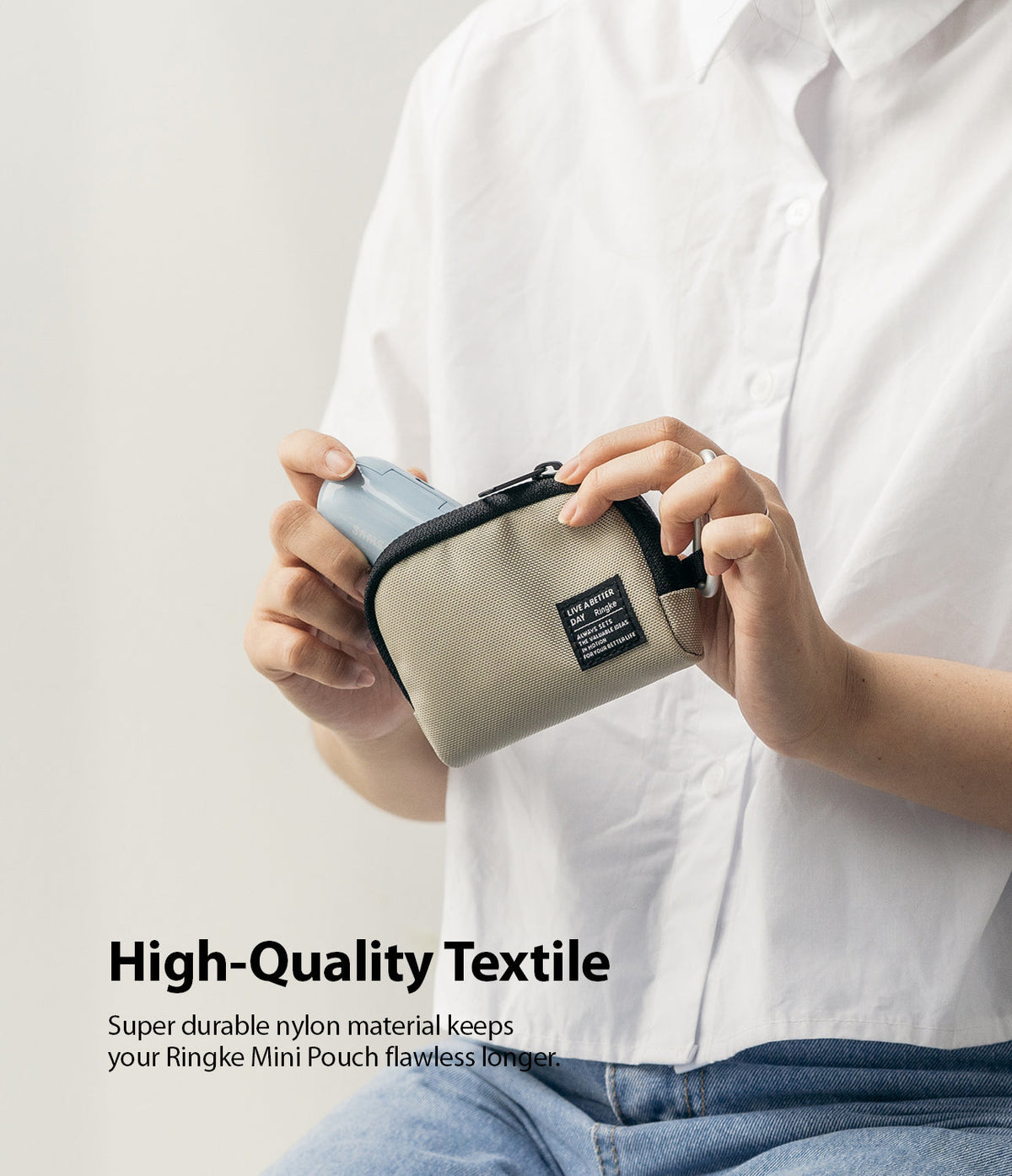 Mini Pouch | Half-Pocket - Person holding a beige nylon mini pouch with a black zipper and a small branded label.