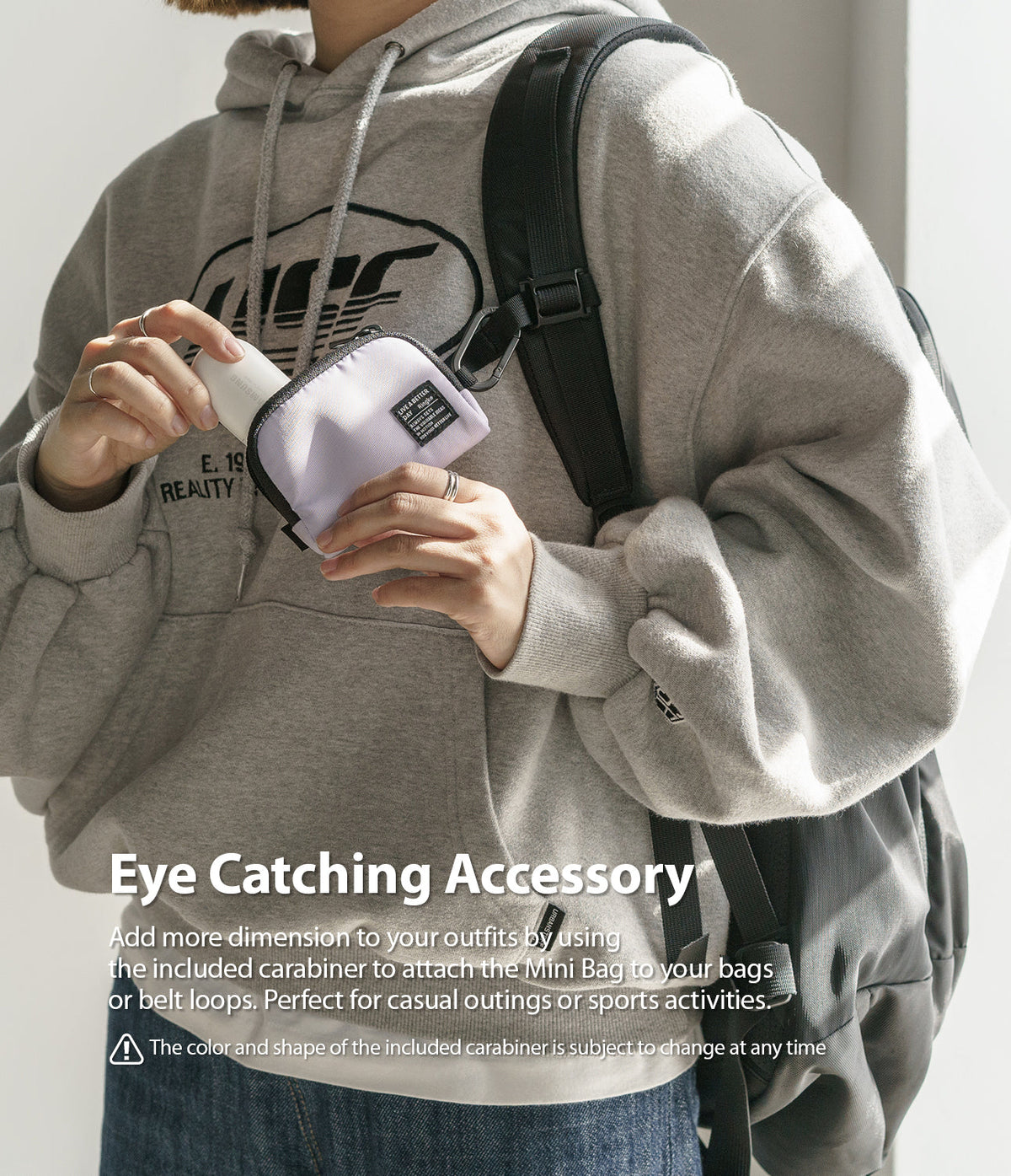 Mini Pouch | Half-Pocket - A person wearing a grey hoodie holds a small lavender pouch attached to their backpack by a carabiner.