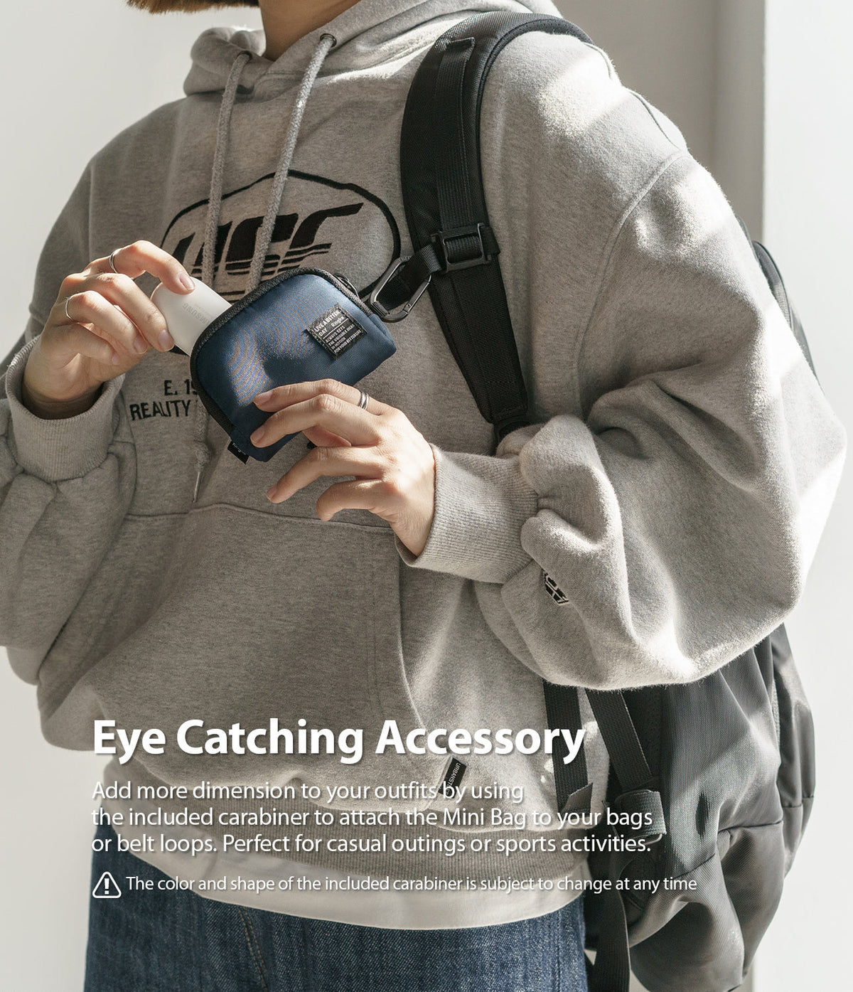 Mini Pouch | Half-Pocket - Person in a grey hoodie holding a navy blue mini pouch attached to a backpack strap by a carabiner.