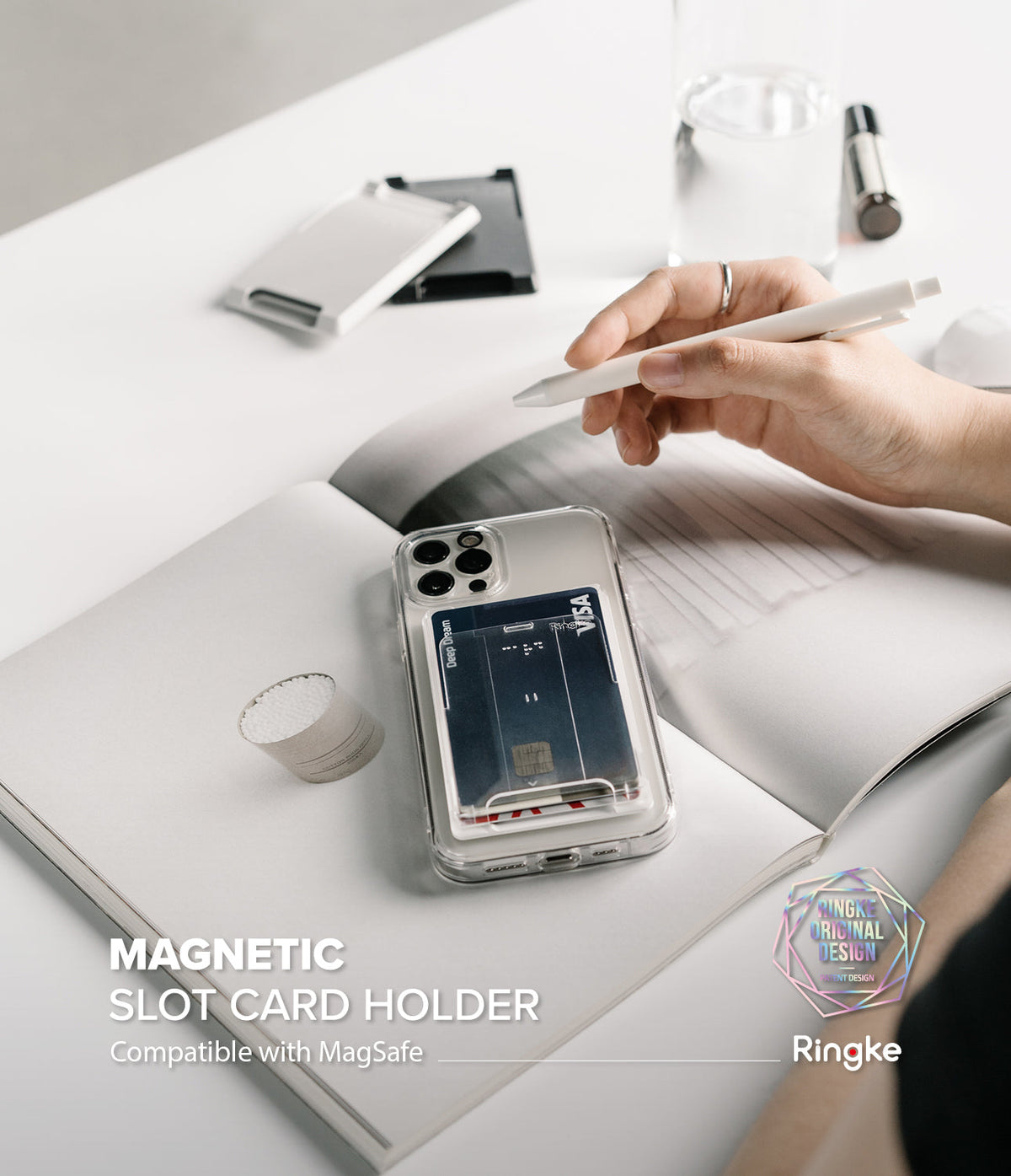 Card Holder | Magnetic Slot - A clear phone case with a magnetic card holder attached, resting on an open notebook with a pen.