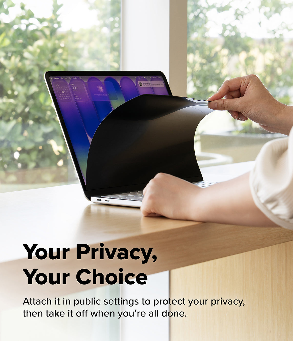 MacBook Neo | Magnetic AG Privacy Film - A person's hands peel off a black privacy film from a laptop screen on a light wood desk, with a blurred outdoor background and the text 'Your Privacy, Your Choice' on the lower left.
