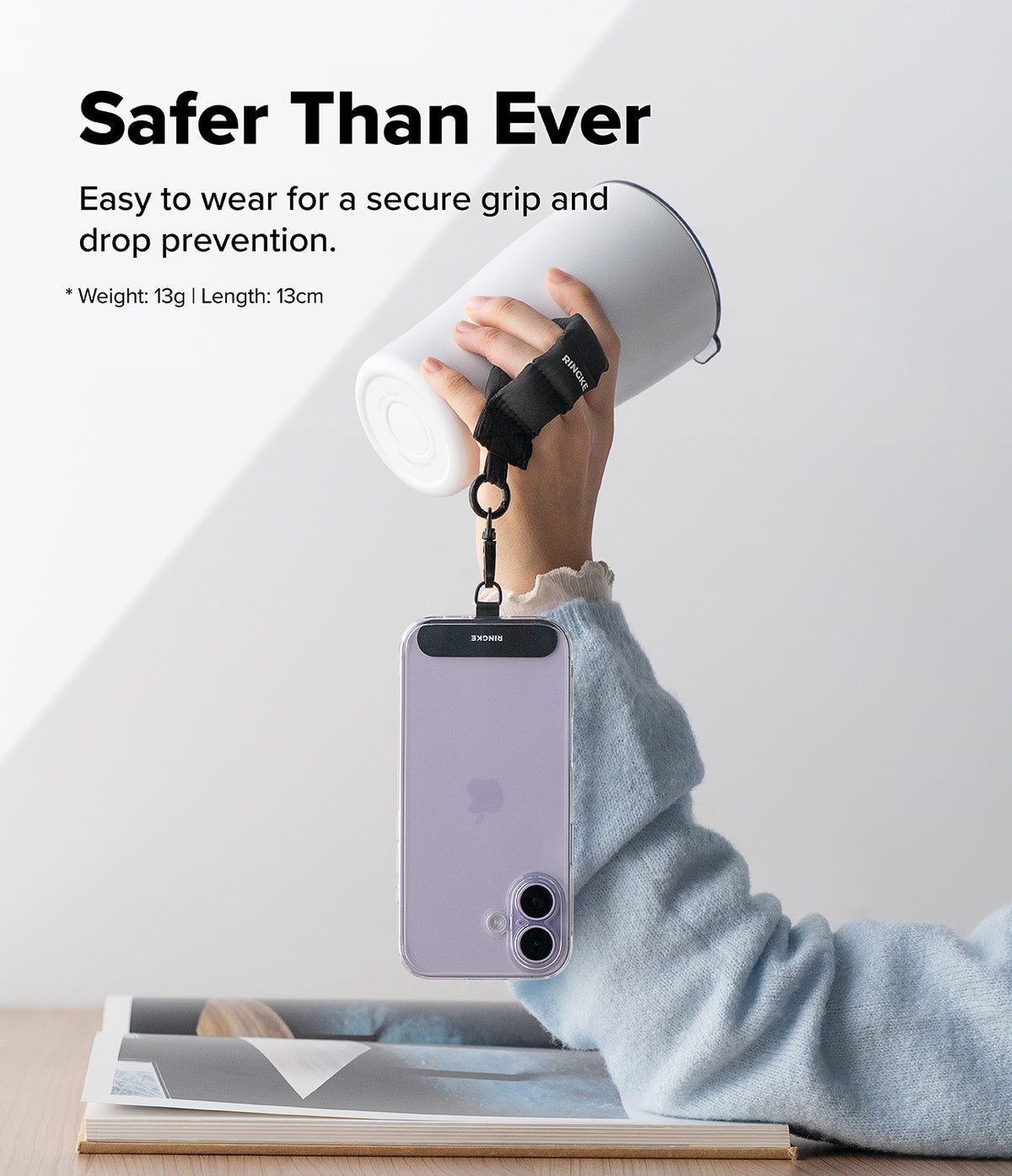 Holder Link Puffer | Finger - A hand holds a white tumbler with a black finger strap attached to a smartphone hanging below.