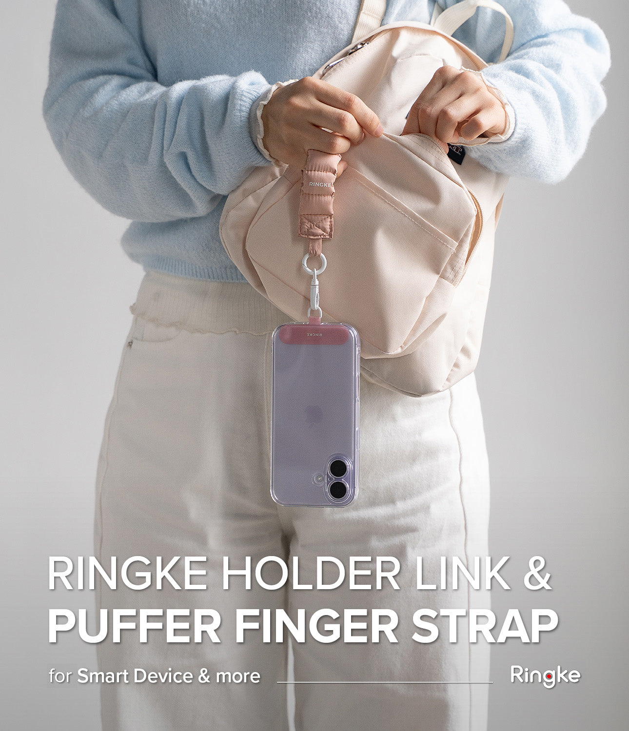 Holder Link Puffer | Finger - A person wearing a light blue sweater holds a pink puffer finger strap attached to a phone.