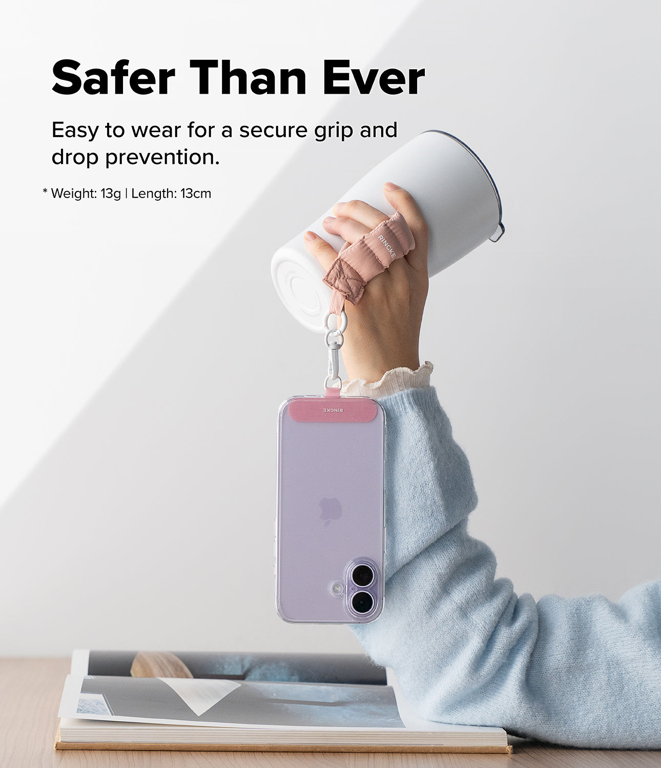 Holder Link Puffer | Finger - A hand wearing a pink puffer finger strap while holding a tumbler and a dangling smartphone.