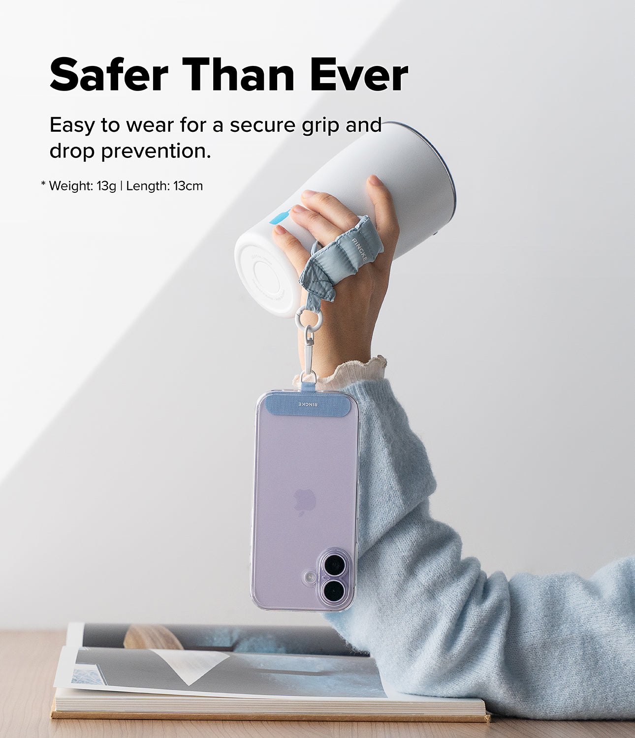 Holder Link Puffer | Finger - A hand holds a white tumbler using a light blue puffer finger strap attached to a phone.