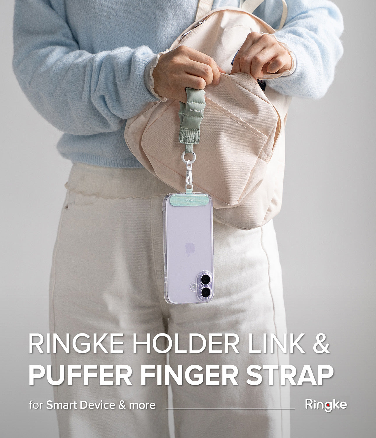 Holder Link Puffer | Finger - A person wearing a light blue sweater holds a sage green puffer finger strap attached to a phone.