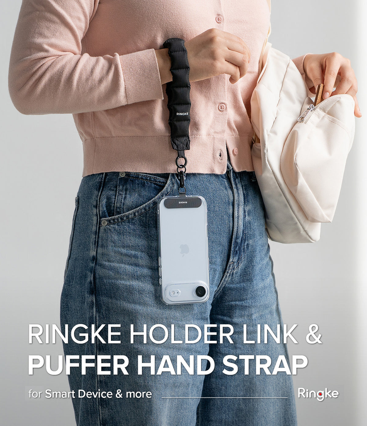 Holder Link Puffer | Hand - A person wearing a black quilted puffer wrist strap attached to a clear phone case hanging at their hip.