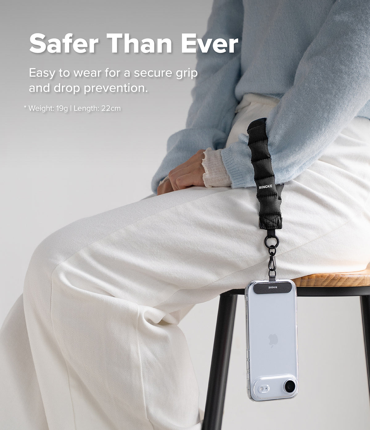 Holder Link Puffer | Hand - Person wearing a black quilted wrist strap attached to a smartphone hanging from their hand.