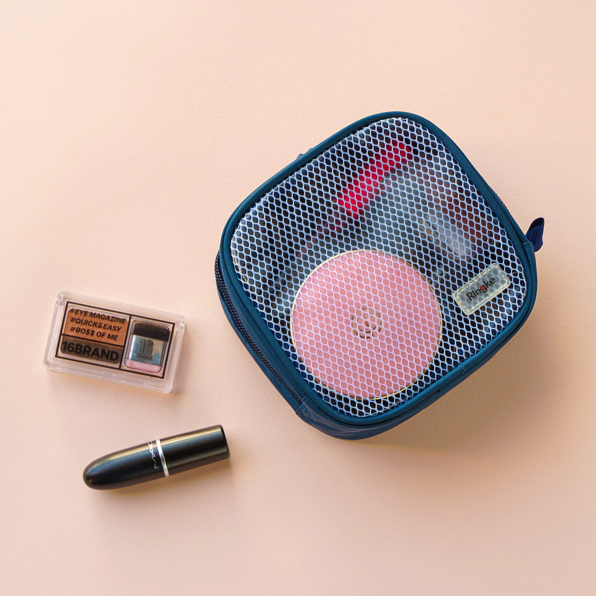 Travel Organizer Pouch - A blue mesh pouch containing a pink compact, next to an eyeshadow palette and a black lipstick.
