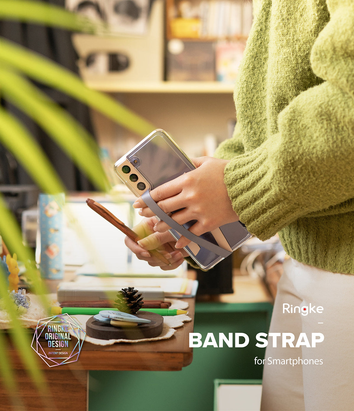 Ringke Strap Band - A person in a green sweater holding a smartphone with a grey finger strap attached to the back.