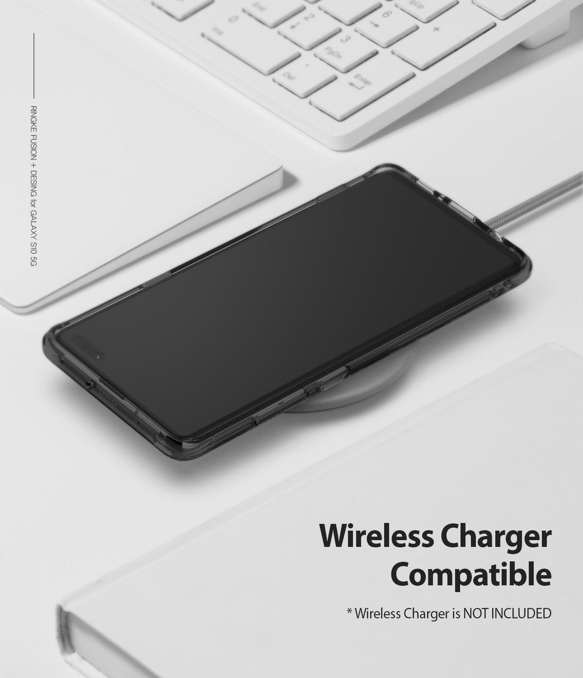 Galaxy S10 5G Case | Fusion - A black-cased smartphone resting on a wireless charging pad near a white keyboard and notebook.