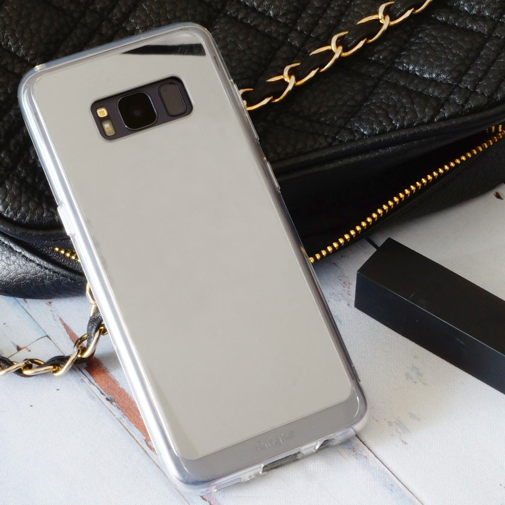 Galaxy S8 Plus Case | Mirror - Reflective silver phone case resting on a white surface next to a black quilted handbag.