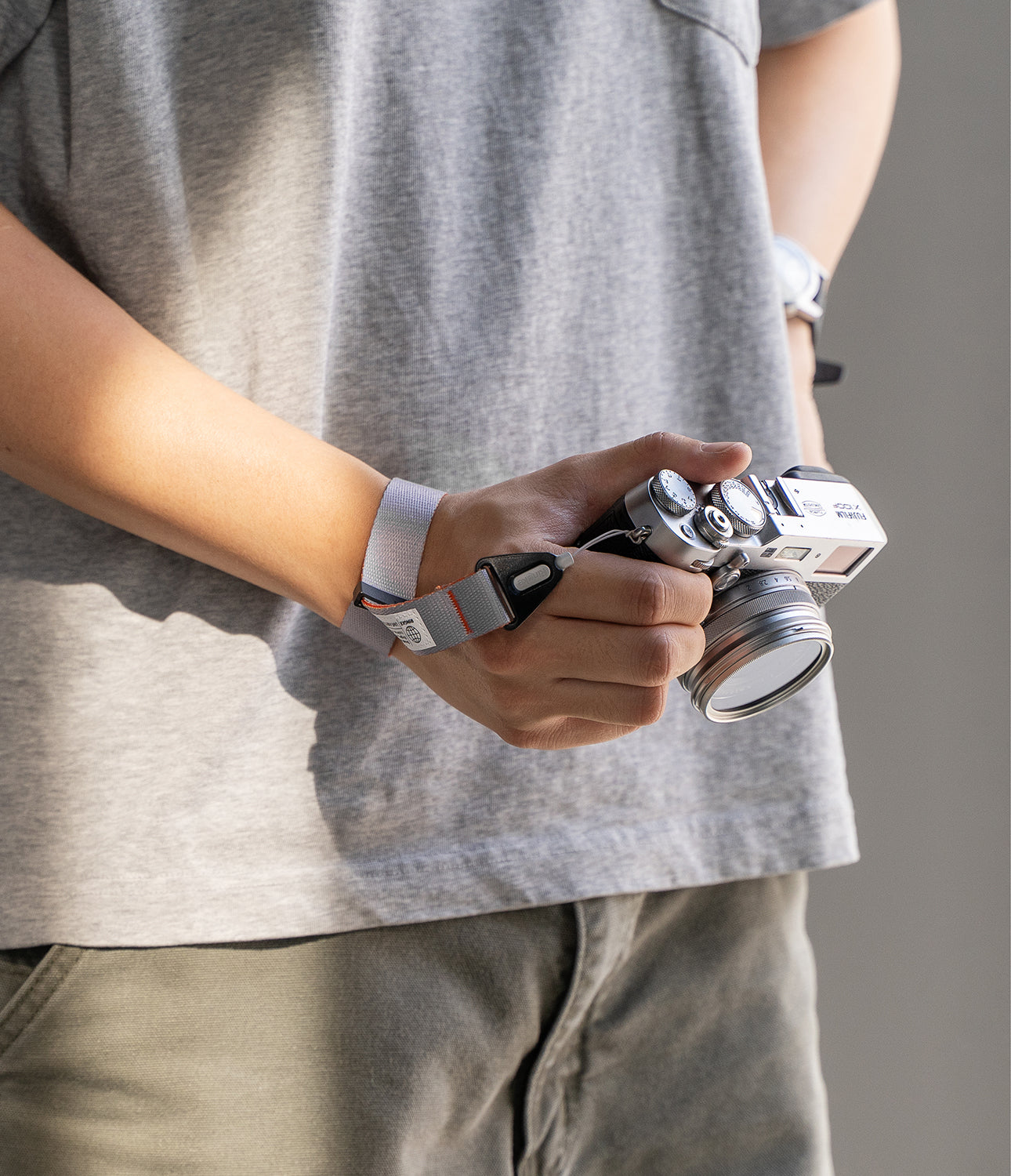 Design Hand Strap - A person wearing a grey wrist strap attached to a silver Fujifilm camera held in their hand.